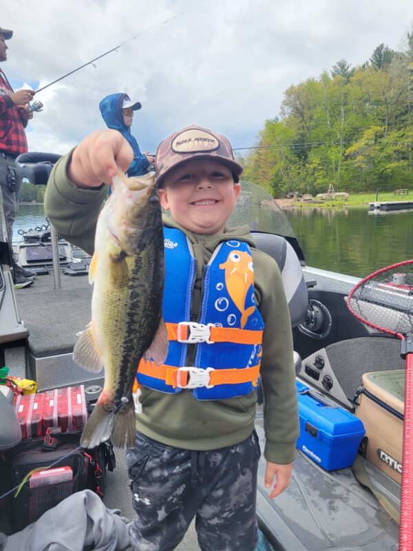Young angler in a life jacket holding a largemouth bass from the bass boat