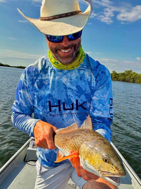 Angler in a straw hat holding a redfish on the flats