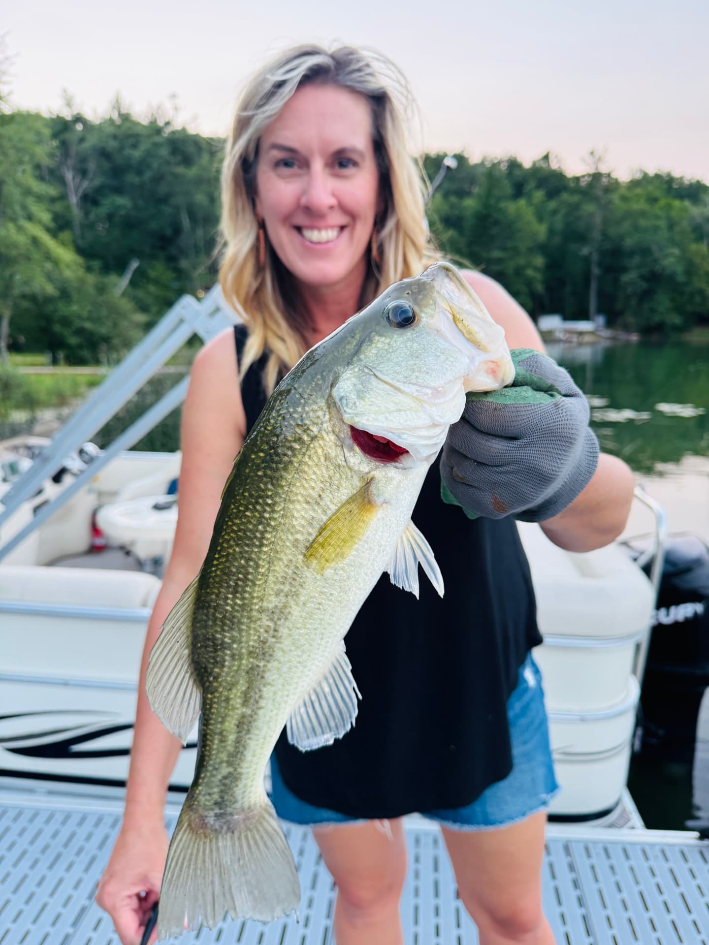 Angler on a pontoon holding a big largemouth bass at dusk