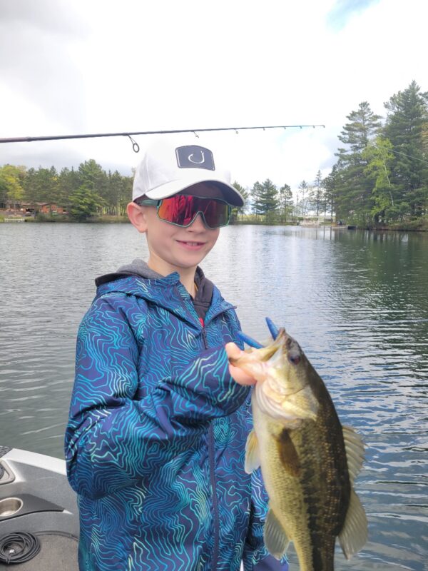 Young angler in sunglasses holding a largemouth bass on the lake
