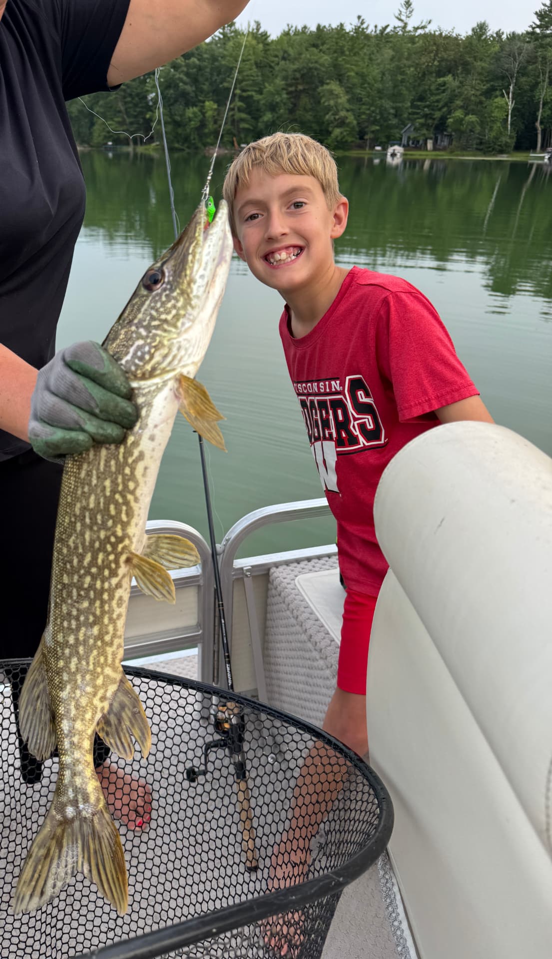 Young angler smiling next to a northern pike in the net