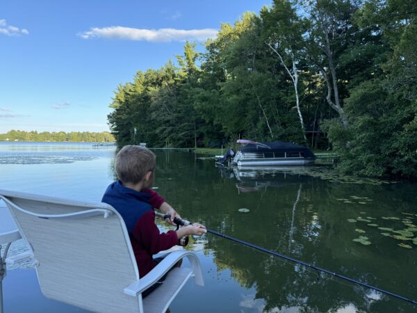 Young angler casting toward a wooded shoreline from the pontoon
