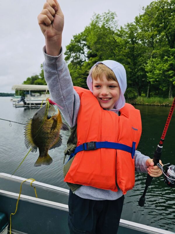 Kid holding up a bluegill caught off the pontoon