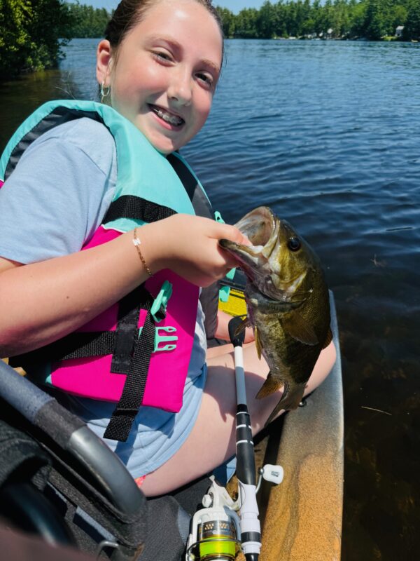 Girl in a kayak holding a smallmouth bass on a sunny lake