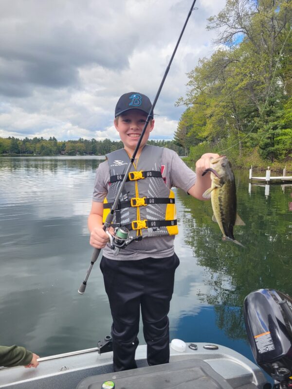 Kid in a life jacket holding a bass on a calm northwoods lake